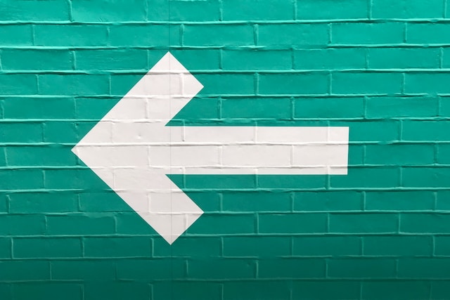 White arrow facing left on green background